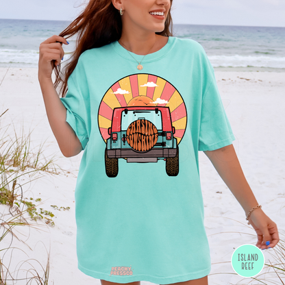 Island Reef Comfort Colors unisex t-shirt featuring a retro off-road vehicle driving toward a vibrant sunset with "Chasing Sunshine" on the spare tire. Vintage beach-inspired graphic in pastel turquoise, coral, and golden yellow, perfect for summer vacations, coastal adventures, road trips, camping, and everyday casual wear.