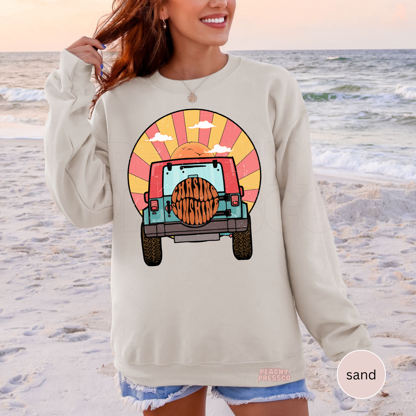 Sand Gildan crewneck sweatshirt featuring a retro off-road vehicle and sunset graphic with "Chasing Sunshine" on the spare tire. Cozy unisex sweatshirt with vintage beach vibes, perfect for cool summer nights, camping trips, vacations, and everyday wear.