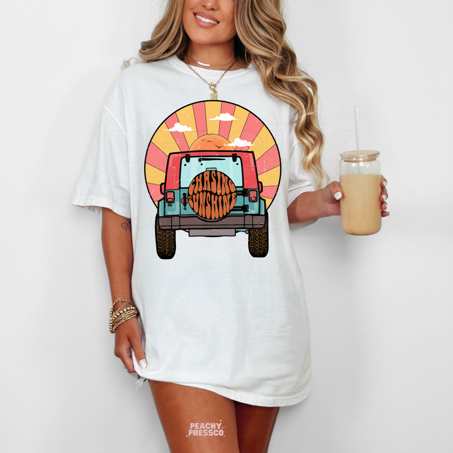 White Gildan unisex t-shirt featuring a retro off-road vehicle driving toward a colorful sunset with "Chasing Sunshine" on the spare tire. Vintage summer graphic tee perfect for beach days, vacations, camping, road trips, and casual everyday wear.