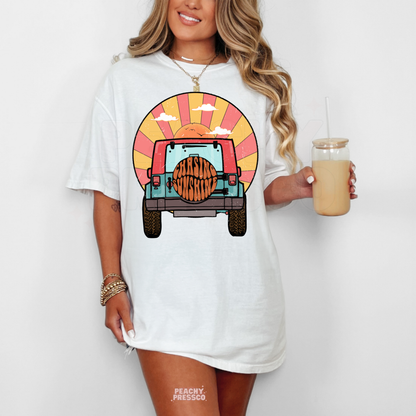White Gildan unisex t-shirt featuring a retro off-road vehicle driving toward a colorful sunset with "Chasing Sunshine" on the spare tire. Vintage summer graphic tee perfect for beach days, vacations, camping, road trips, and casual everyday wear.