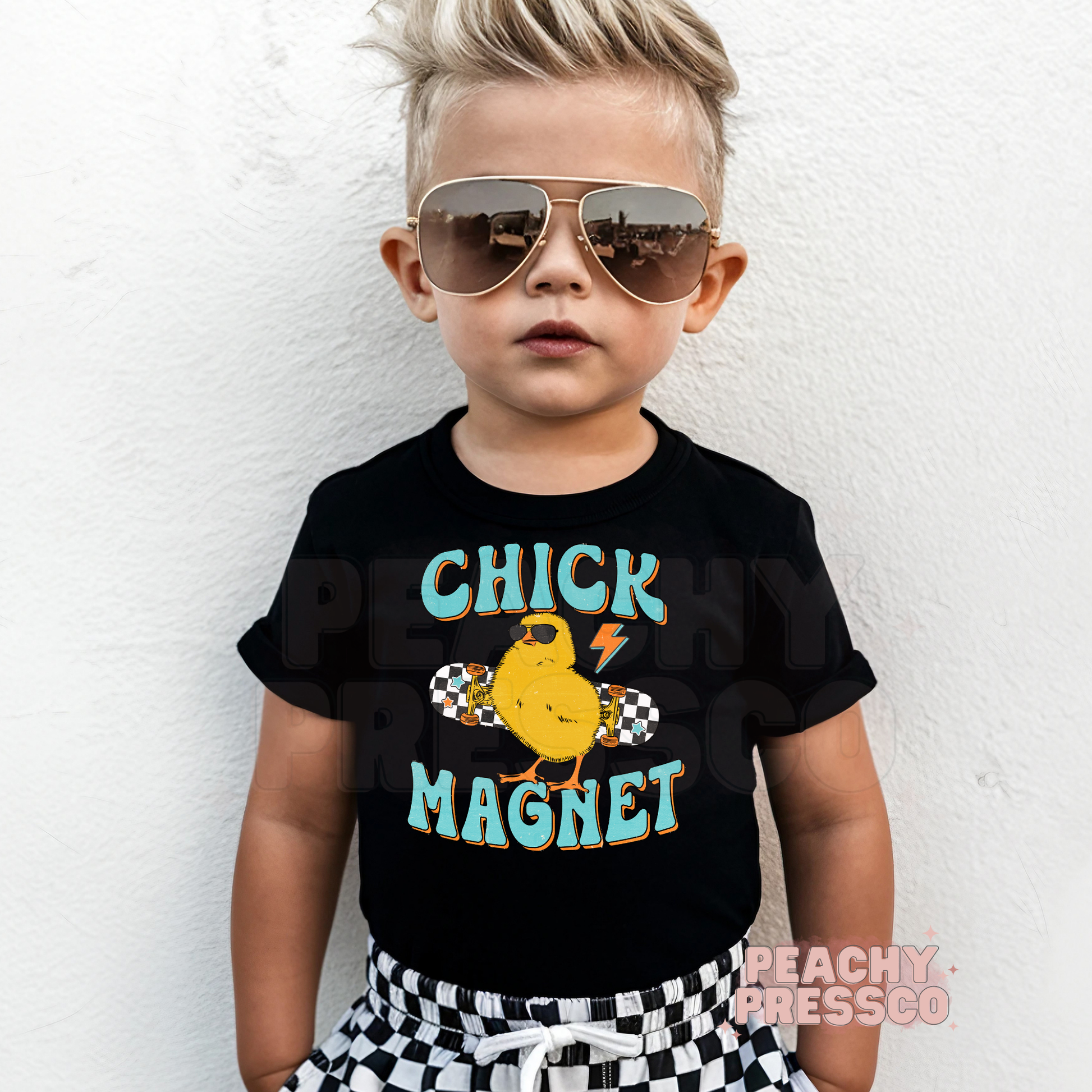 Toddler boy wearing a black Chick Magnet Easter shirt featuring a cool chick with sunglasses on a skateboard.
