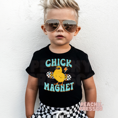 Toddler boy wearing a black Chick Magnet Easter shirt featuring a cool chick with sunglasses on a skateboard.