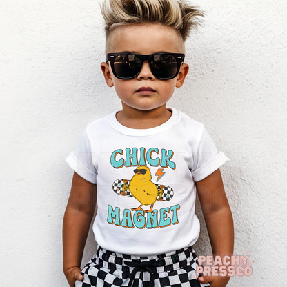 Toddler boy wearing a white Chick Magnet Easter shirt with a retro skateboard chick graphic and playful Easter theme.