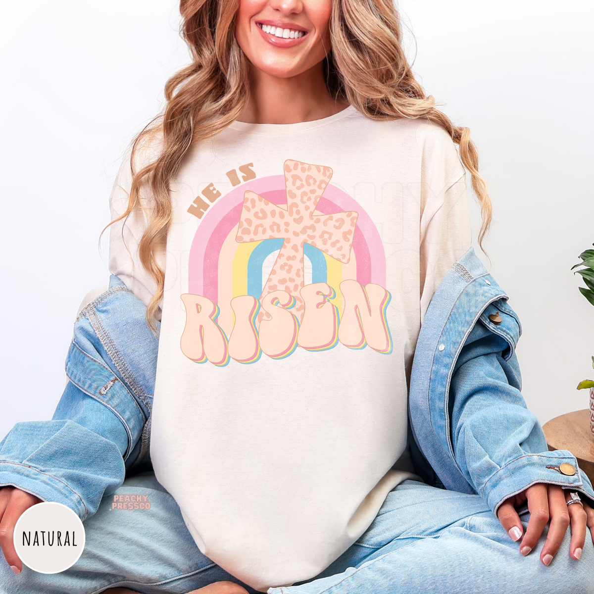 Natural shirt featuring a pastel rainbow, leopard-print cross, and retro "He Is Risen" graphic. Cozy Christian Easter sweatshirt perfect for church, spring, and everyday faith.