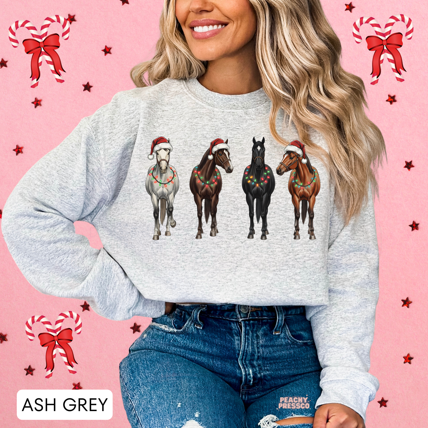 Women wearing an ash grey Christmas horse sweatshirt tucked into jeans, set against a pink holiday accent background.