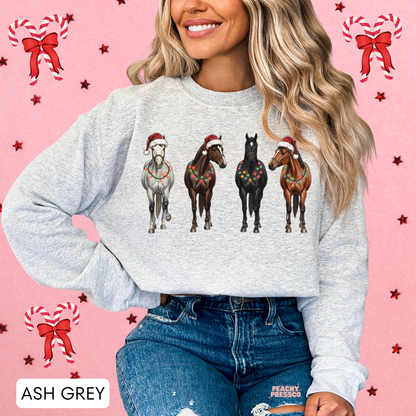 Women wearing an ash grey Christmas horse sweatshirt tucked into jeans, set against a pink holiday accent background.