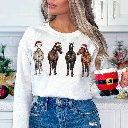 Women in a kitchen holding a Santa ceramic mug and wearing a white crewneck sweatshirt printed with horses wrapped in Christmas lights.