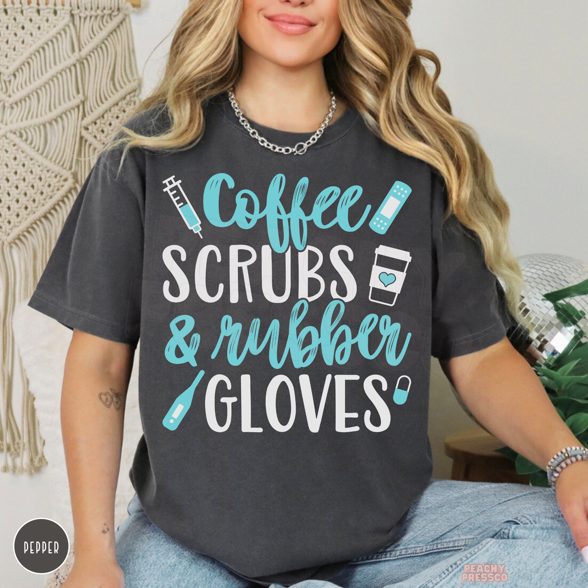 Woman modeling a pepper charcoal T-shirt with Coffee Scrubs & Rubber Gloves design, turquoise lettering and medical illustrations.
