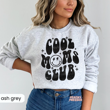Ash Grey sweatshirt displaying the "Cool Moms Club" retro graphic with a smiley face and distressed black print. Comfortable everyday mom crewneck.
