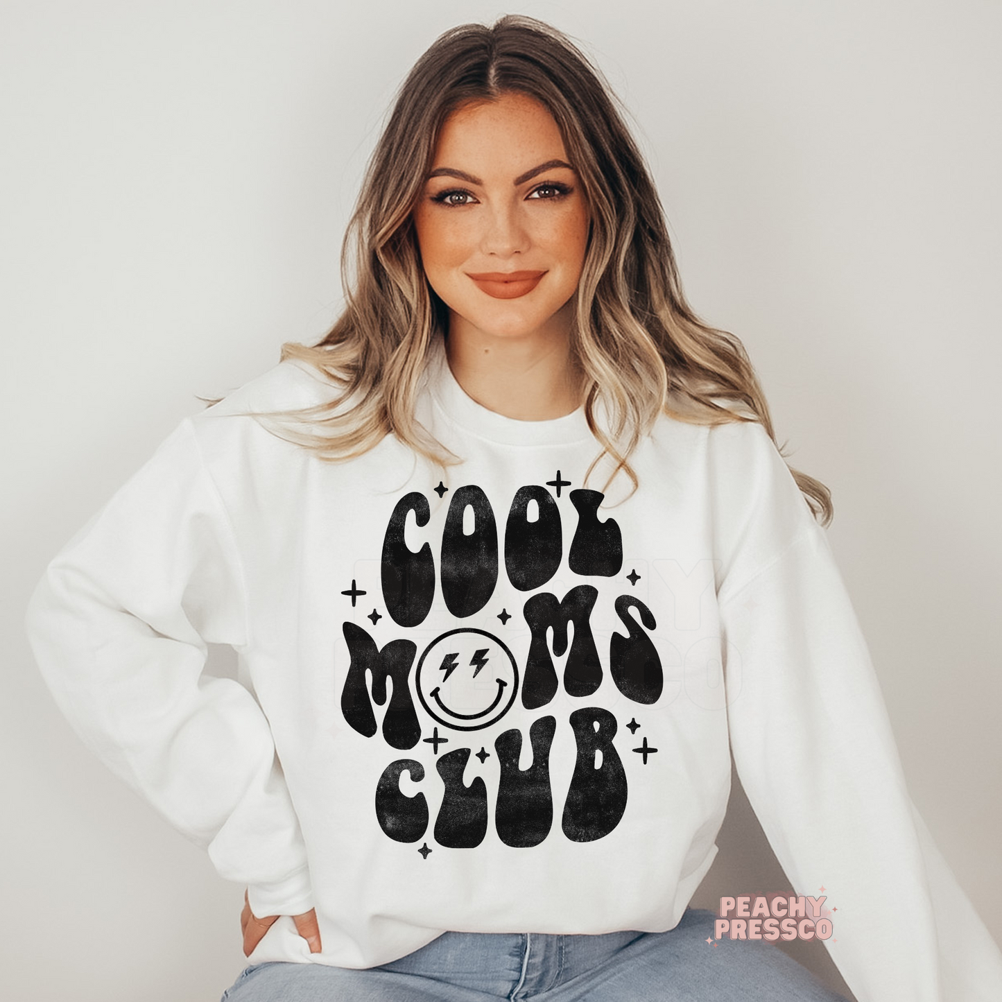 White sweatshirt featuring a retro "Cool Moms Club" graphic with a smiley face and vintage black lettering. Trendy graphic sweatshirt for stylish moms.