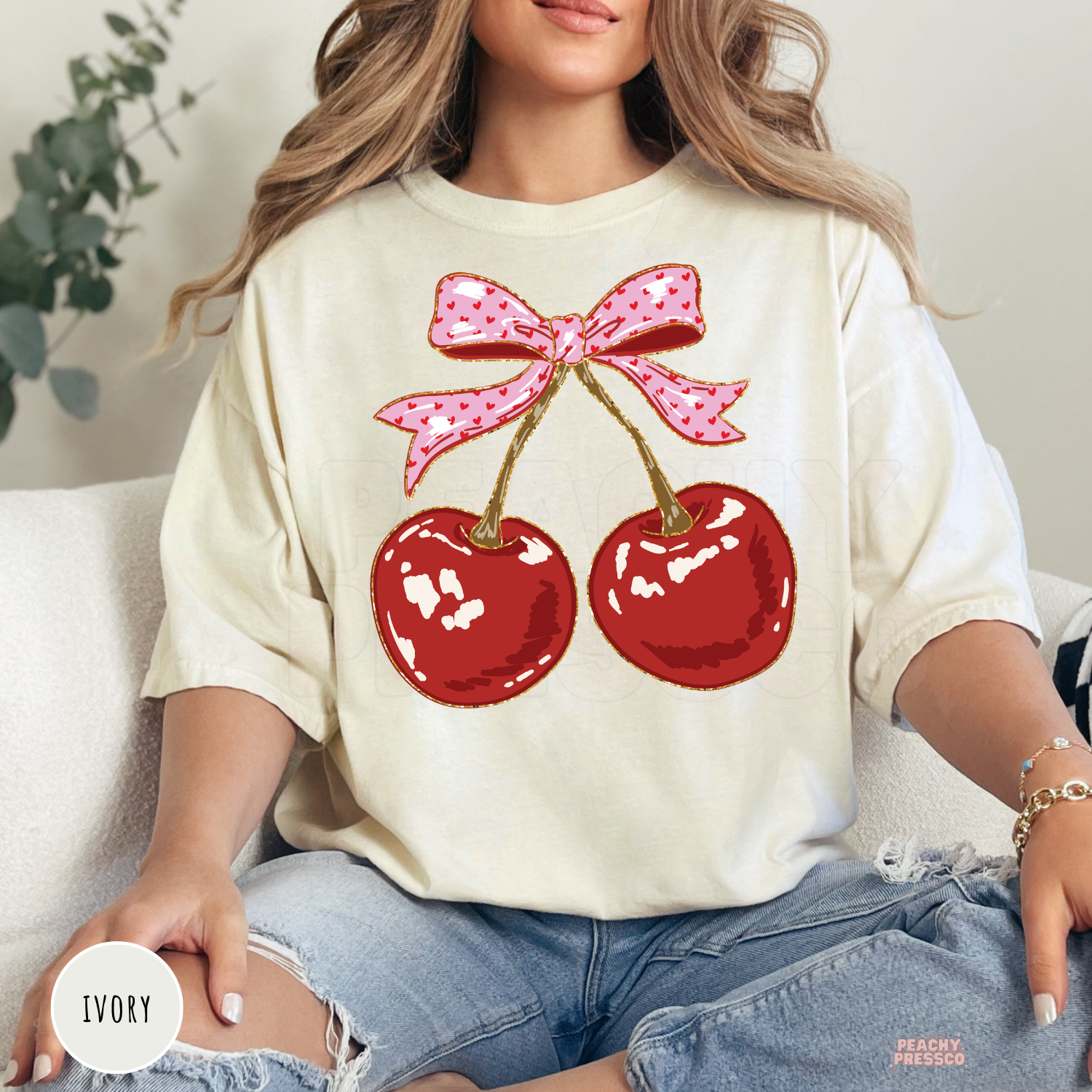 Ivory Comfort Colors t-shirt with a coquette cherry graphic featuring two red cherries tied with a pink ribbon bow, trendy women's graphic tee.