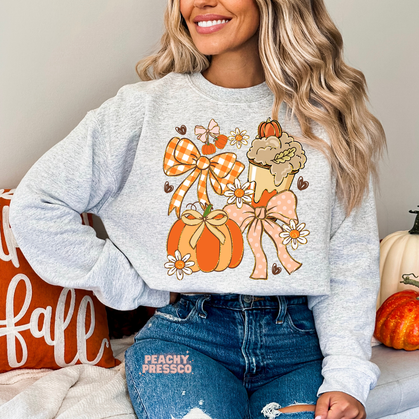 Woman wearing an ash grey crewneck sweatshirt featuring a cute coquette fall design with pumpkins, bows, daisies and a pumpkin spice coffee.