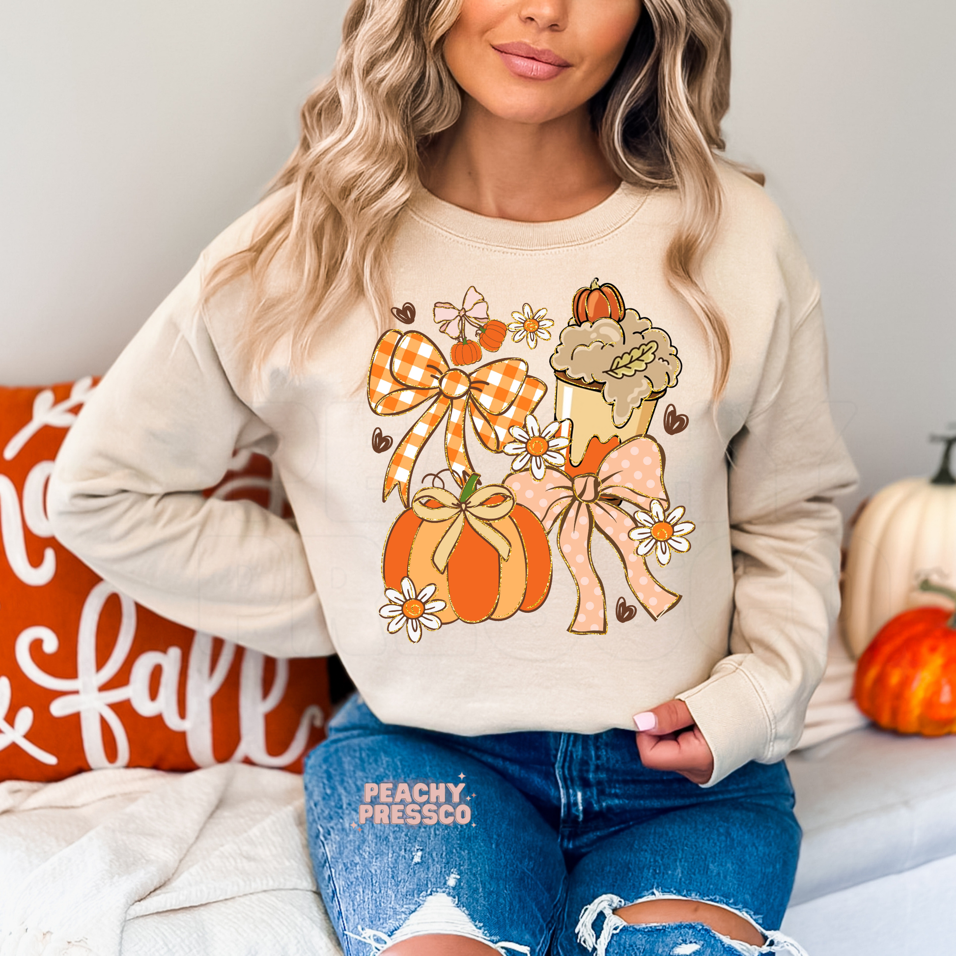 Woman wearing a sand crewneck sweatshirt with a cute coquette fall graphic featuring pumpkins, gingham bow, pink bow, flowers and a pumpkin spice coffee.
