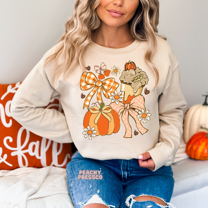 Woman wearing a sand crewneck sweatshirt with a cute coquette fall graphic featuring pumpkins, gingham bow, pink bow, flowers and a pumpkin spice coffee.