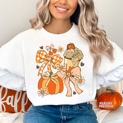 Woman wearing a white crewneck sweatshirt featuring a cute coquette pumpkin and bow graphic with daisies and a pumpkin spice coffee for fall.