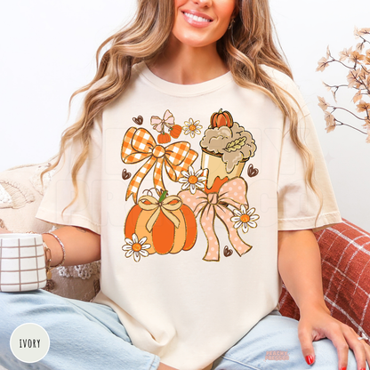 Woman wearing an ivory graphic t-shirt featuring a coquette autumn design with pumpkins, bows, daisies and a pumpkin spice latte.