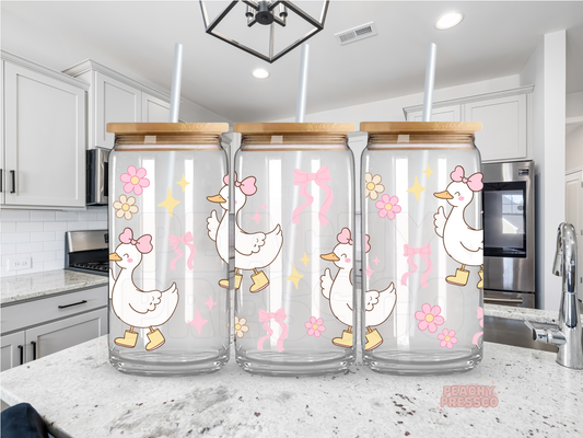 Cute glass can featuring adorable geese wearing pink bows and rain boots with pink flowers, bows, and sparkles on a clear iced coffee tumbler.
