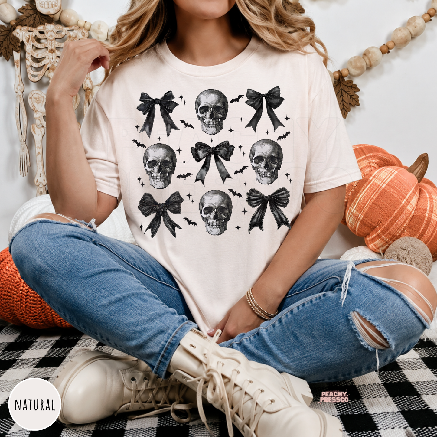 Woman wearing a natural graphic t-shirt with black bows, skulls and bats in a coquette Halloween design, perfect for spooky season.