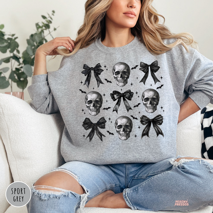 Woman wearing a sport grey crewneck sweatshirt featuring black bows, vintage skulls and bats in a trendy coquette Halloween design.