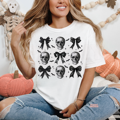 Woman wearing a white Halloween graphic t-shirt featuring coquette skulls, black bows and bats in a cute gothic aesthetic.