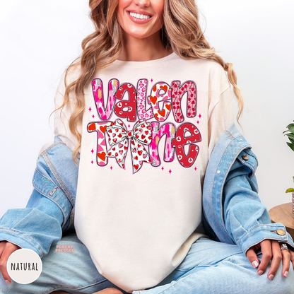 Natural shirt showcasing a colorful stacked "Valentine" design with a heart-pattern bow for Valentine's Day.