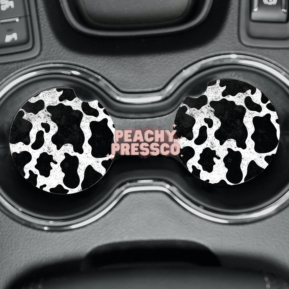 Black and white cow print ceramic car coasters displayed in vehicle cup holders.