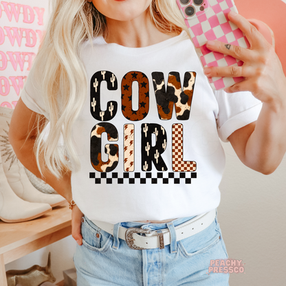 Cowgirl western graphic printed on a white t-shirt featuring cow print, cactus, lightning bolts, checkerboard, and western-inspired lettering.