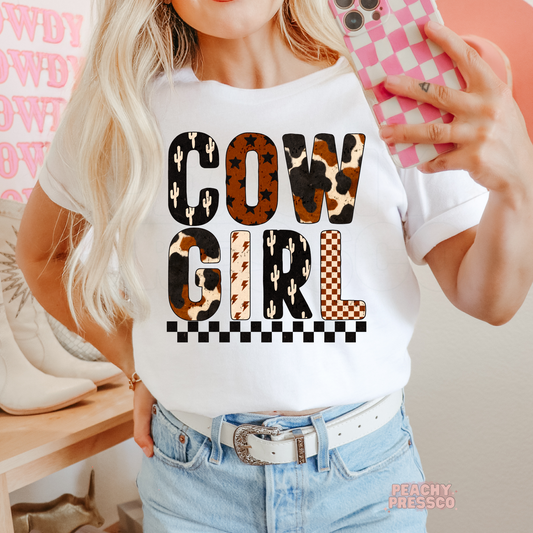 Cowgirl western graphic printed on a white t-shirt featuring cow print, cactus, lightning bolts, checkerboard, and western-inspired lettering.