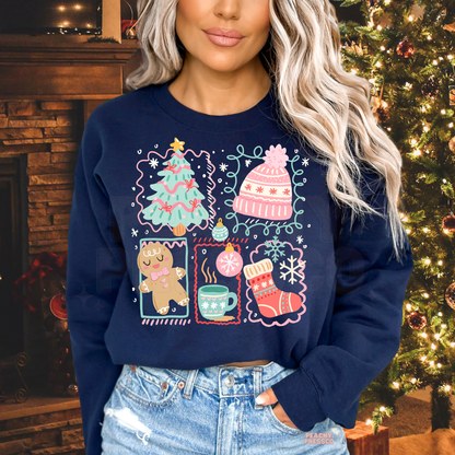 A woman wearing a navy blue crewneck sweatshirt with a colorful Christmas-themed graphic print featuring a tree, hat, gingerbread man, mug, and stocking, posed in front of a decorated Christmas tree and fireplace.