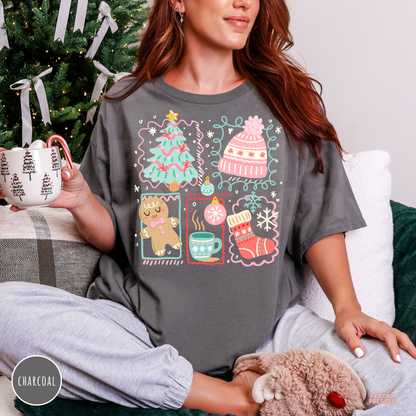 A woman wearing a charcoal gray graphic t-shirt with a Christmas-themed print, sitting on a couch next to a decorated Christmas tree and holding a mug.