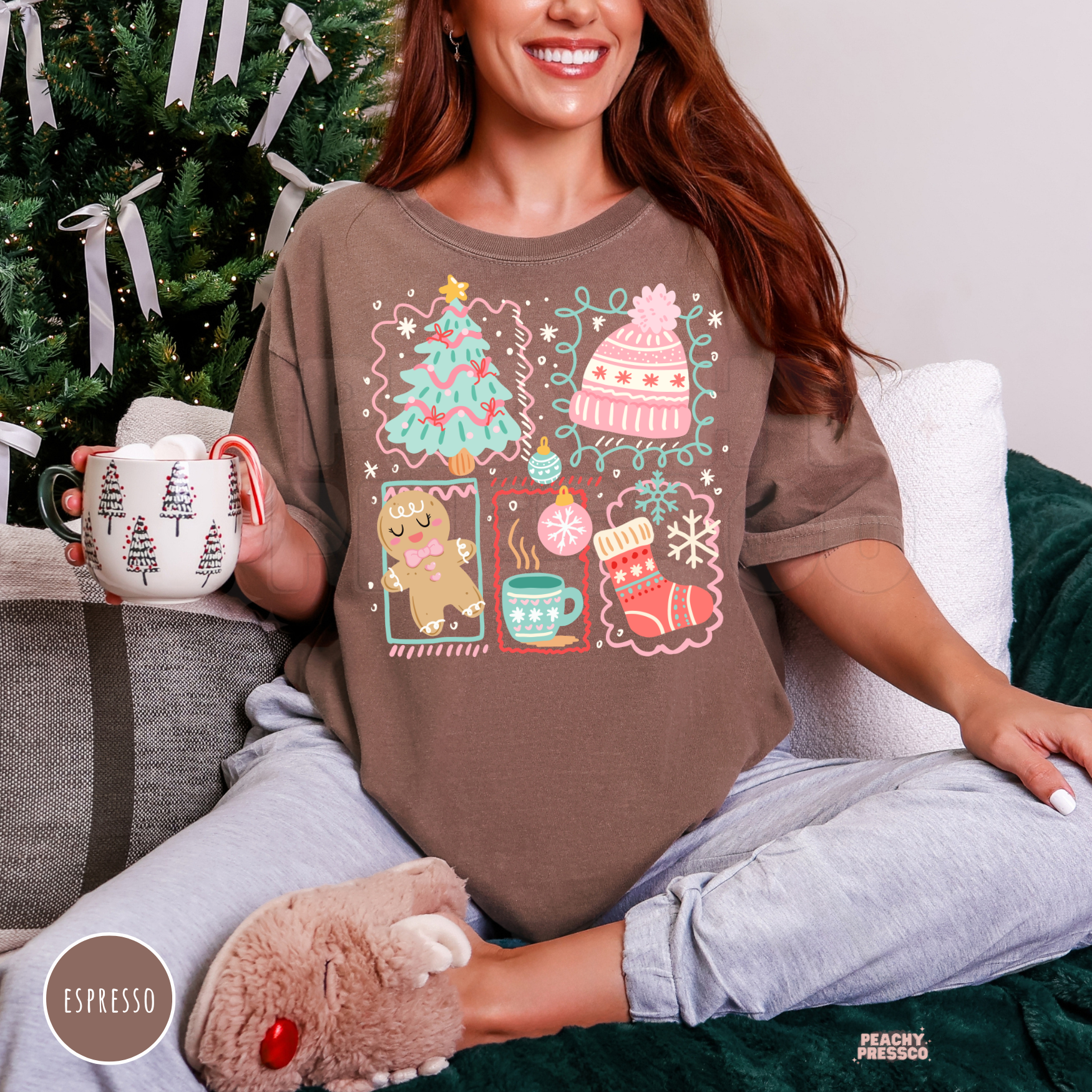 Woman holding a marshmallow hot cocoa mug wearing an espresso brown oversized graphic t-shirt printed with festive holiday collage doodles.