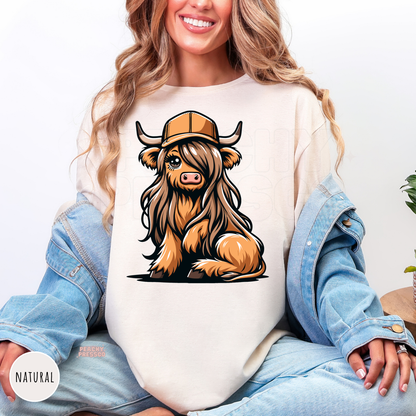 Adorable Highland cow wearing a trucker hat printed on a natural western country shirt.