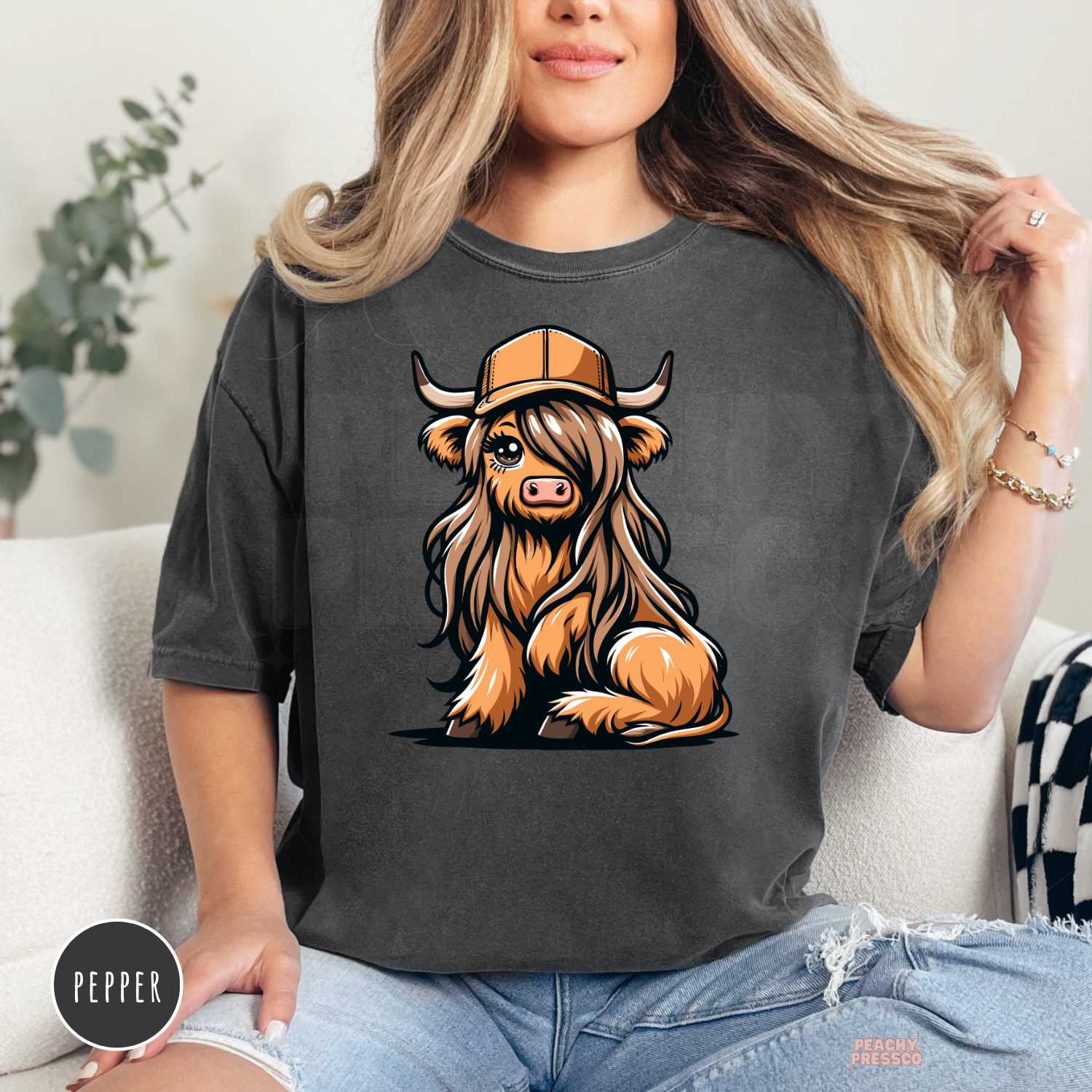 Cute Highland cow with long shaggy hair and trucker hat printed on a pepper Comfort Colors western graphic tee.