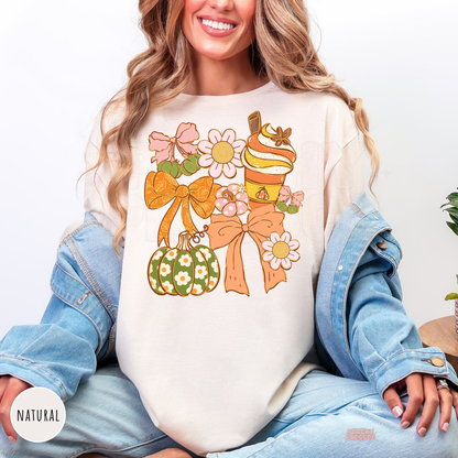 Woman wearing a natural graphic t-shirt with a coquette autumn design featuring bows, pumpkin spice latte, decorative pumpkin, daisies, and trendy fall aesthetic illustration.