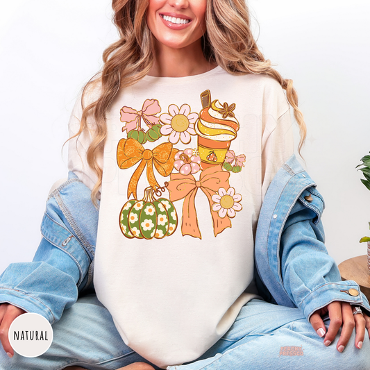 Woman wearing a natural graphic t-shirt with a coquette autumn design featuring bows, pumpkin spice latte, decorative pumpkin, daisies, and trendy fall aesthetic illustration.