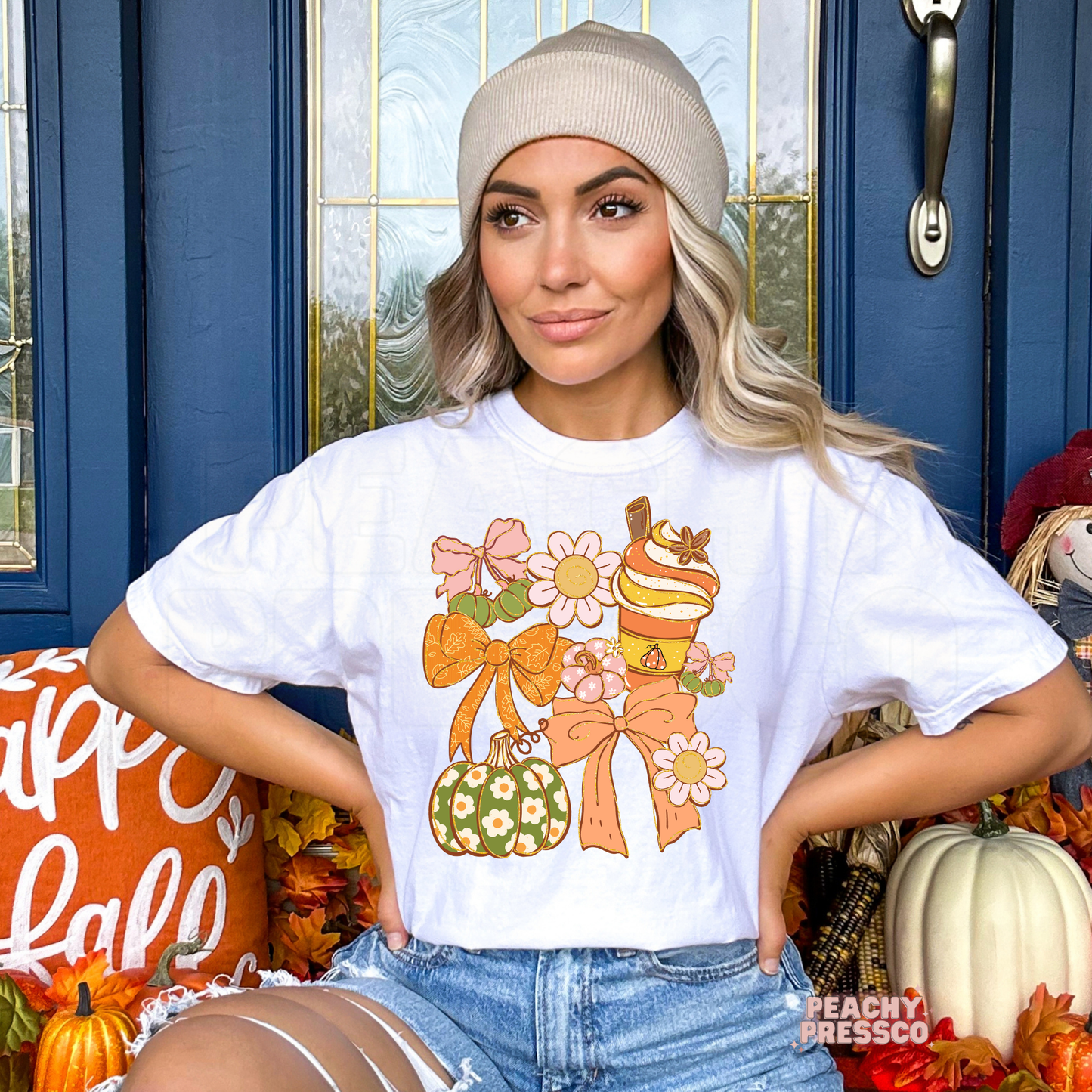 Woman wearing a white graphic t-shirt featuring a coquette fall design with pastel bows, pumpkin spice drink, floral pumpkin, daisy flowers, and cute autumn graphics.