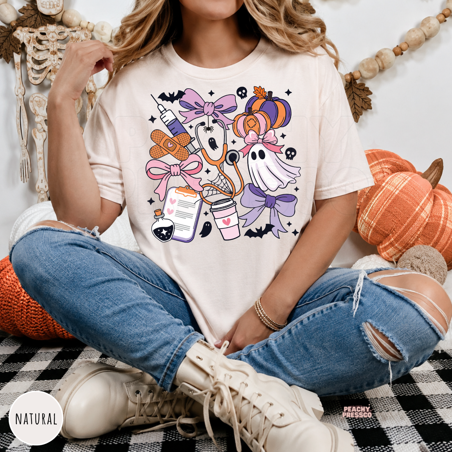 Woman wearing a natural Comfort Colors t-shirt with a cute Halloween nurse design featuring ghosts, pumpkins, stethoscope and medical icons.