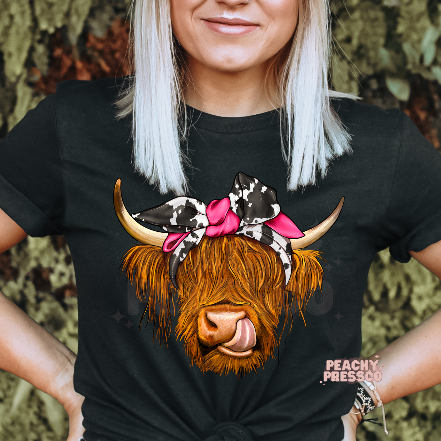 Black t-shirt featuring a funny Highland cow wearing a cow print bandana with a pink bow in a trendy western country style.
