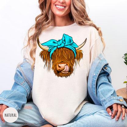 Woman wearing a natural shirt featuring a Highland cow graphic with a turquoise headband bow and rustic western style.