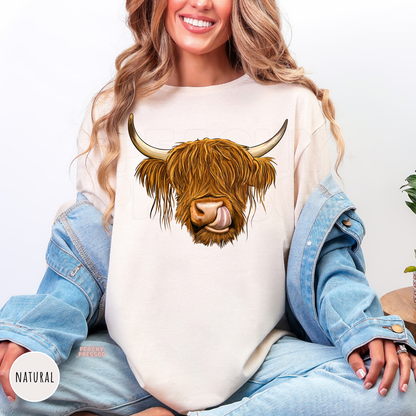 Woman wearing a natural-colored shirt featuring a Highland cow graphic with long shaggy hair and rustic farmhouse style.