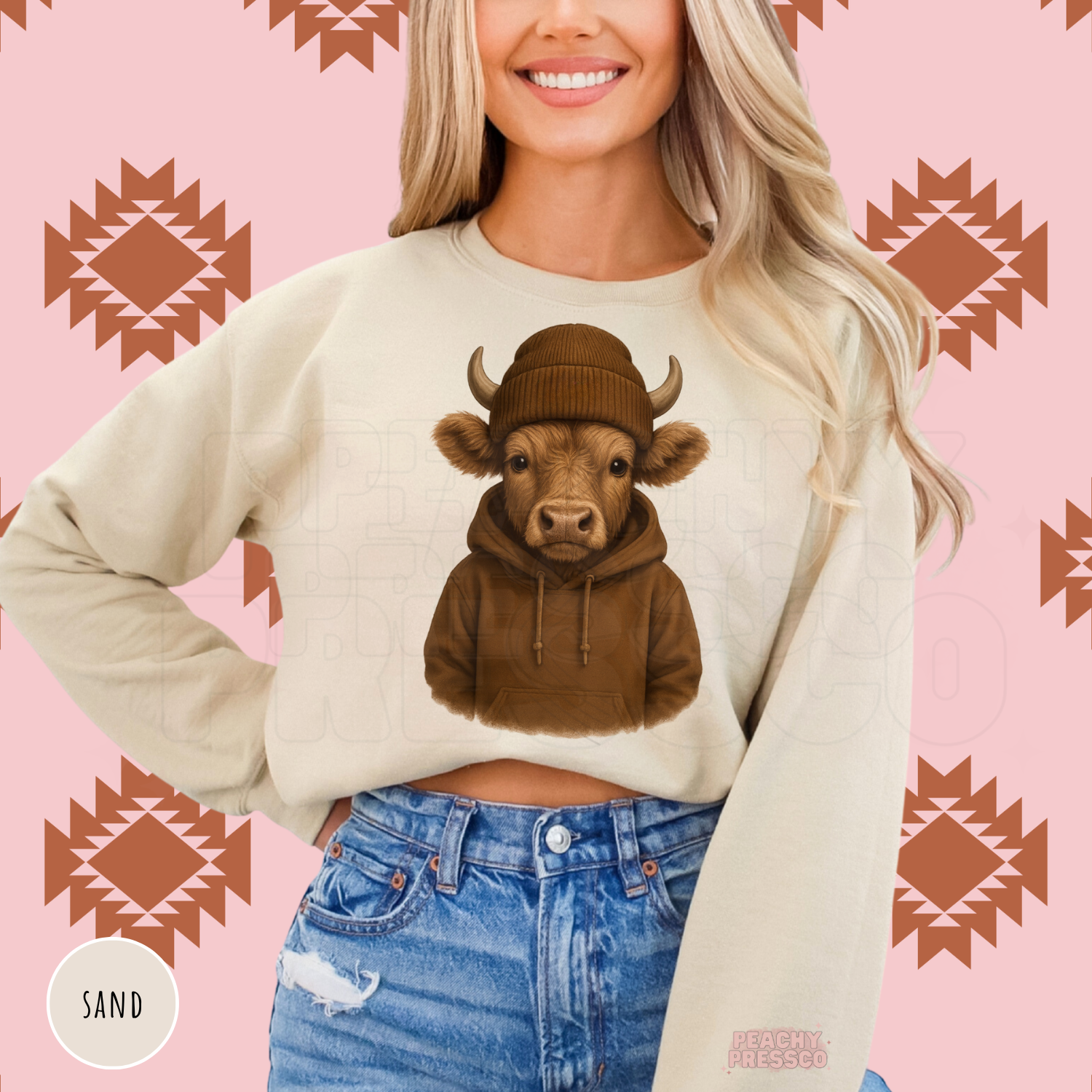 Woman wearing a sand sweatshirt featuring an adorable Highland cow in a brown hoodie and knit beanie, cozy western country graphic.