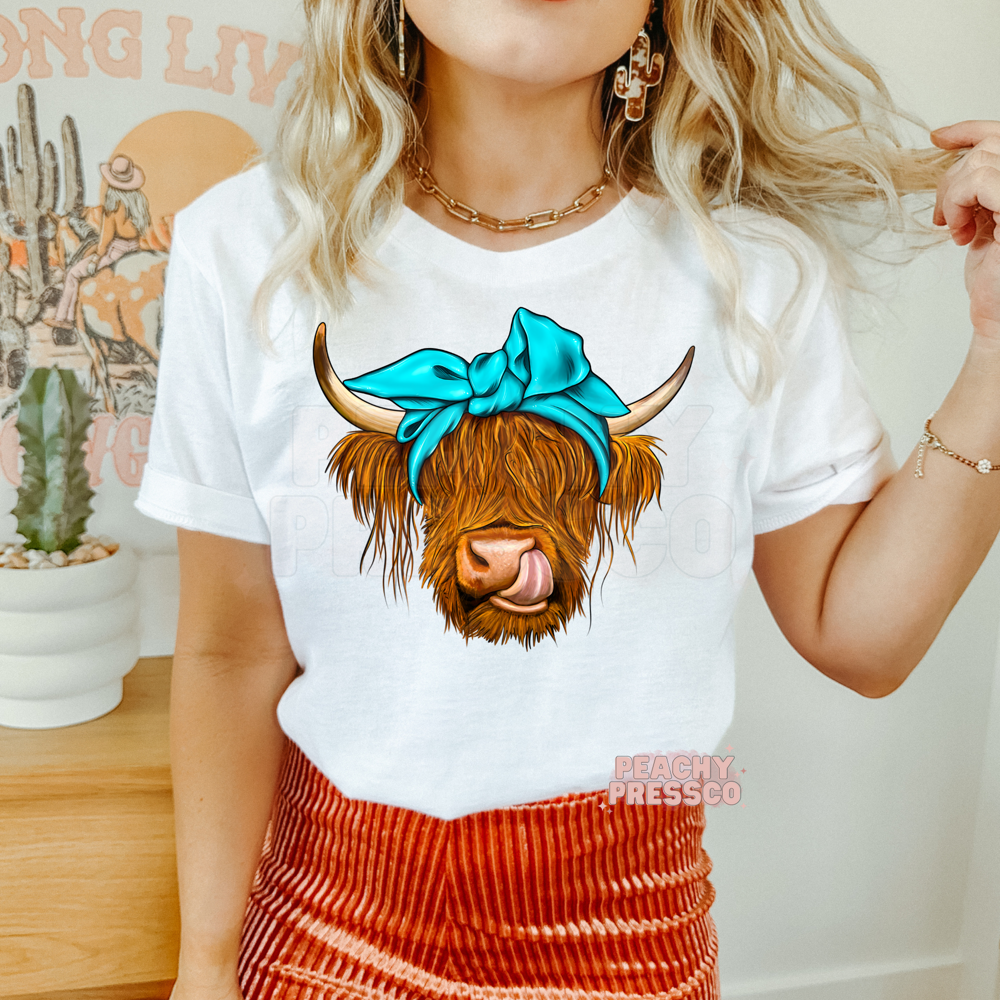 Woman wearing a white graphic t-shirt featuring a Highland cow with a turquoise bow, ideal for western and country fashion.
