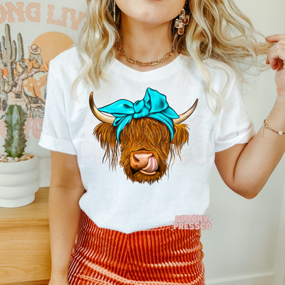 Woman wearing a white graphic t-shirt featuring a Highland cow with a turquoise bow, ideal for western and country fashion.