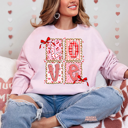 Light pink sweatshirt featuring a romantic LOVE patchwork design with decorative bows, heart patterns, and feminine coquette Valentine's artwork.
