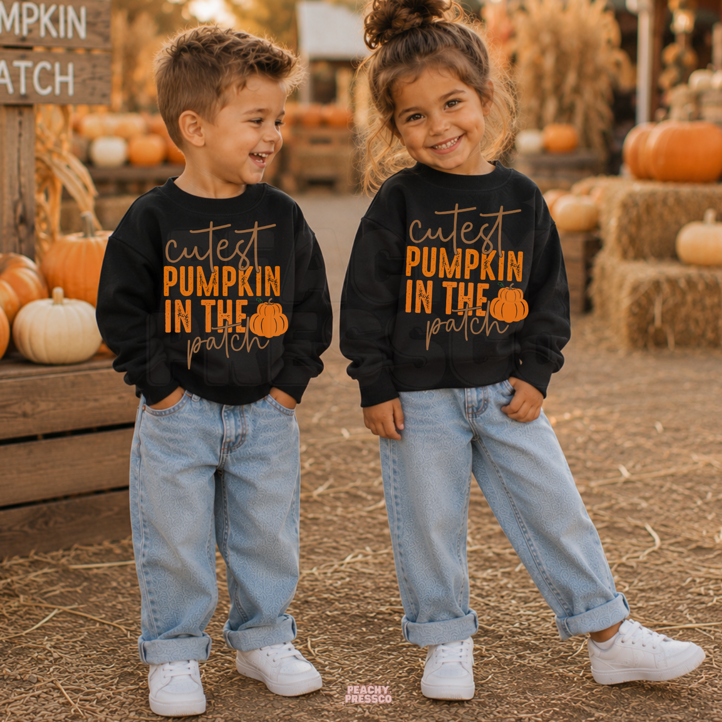 Toddler boy and girl wearing matching black crewneck sweatshirts with a "Cutest Pumpkin in the Patch" graphic at a fall pumpkin patch.

