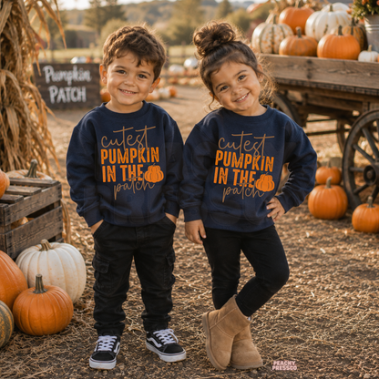 Toddler boy and girl wearing matching navy "Cutest Pumpkin in the Patch" crewneck sweatshirts at a pumpkin patch with pumpkins and fall décor.