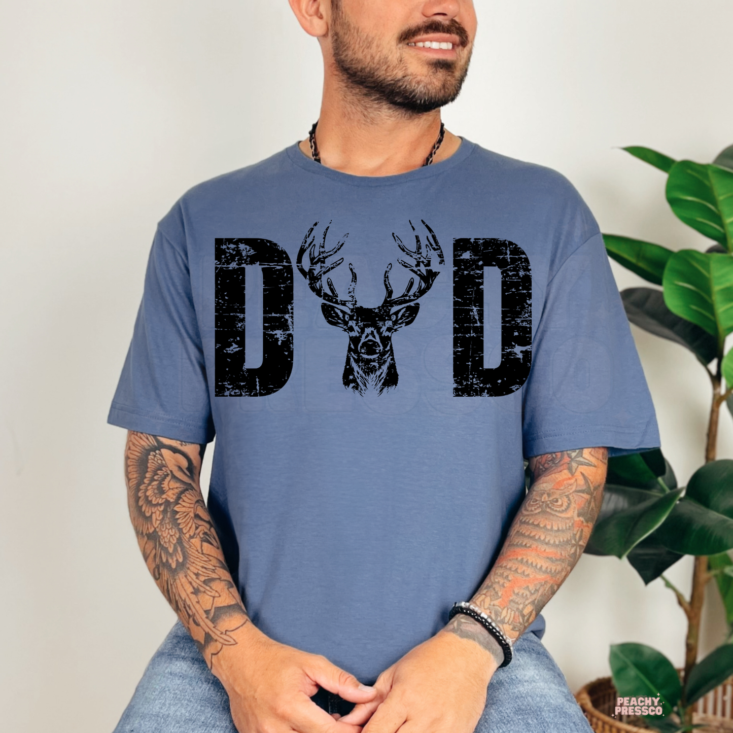 Indigo Blue t-shirt featuring a rustic distressed "DAD" graphic with a detailed buck deer illustration. Great gift for hunting dads, outdoorsmen, and nature enthusiasts.