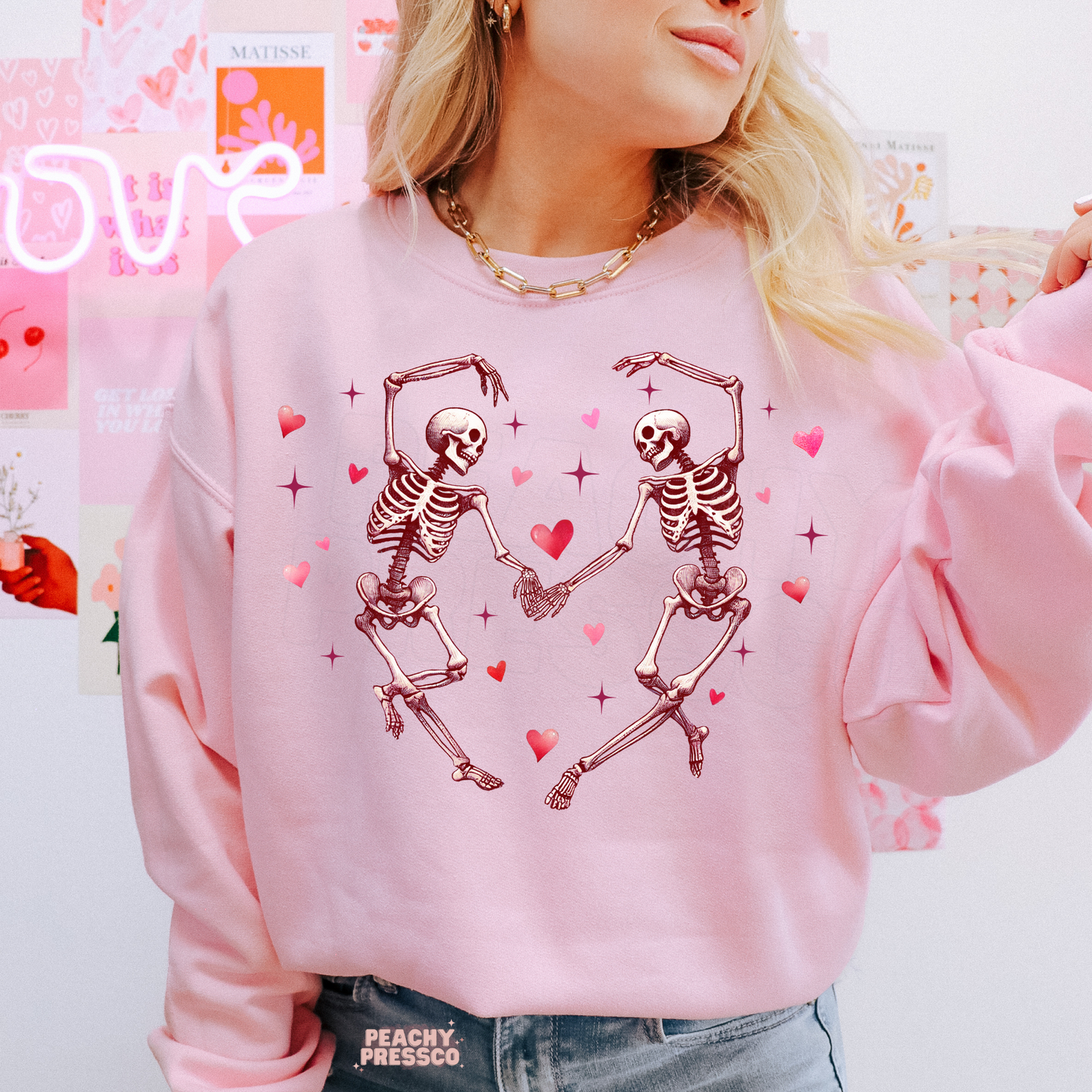 Light pink crewneck sweatshirt displaying a cute dancing skeleton couple surrounded by hearts, ideal for Valentine's Day or Halloween lovers.