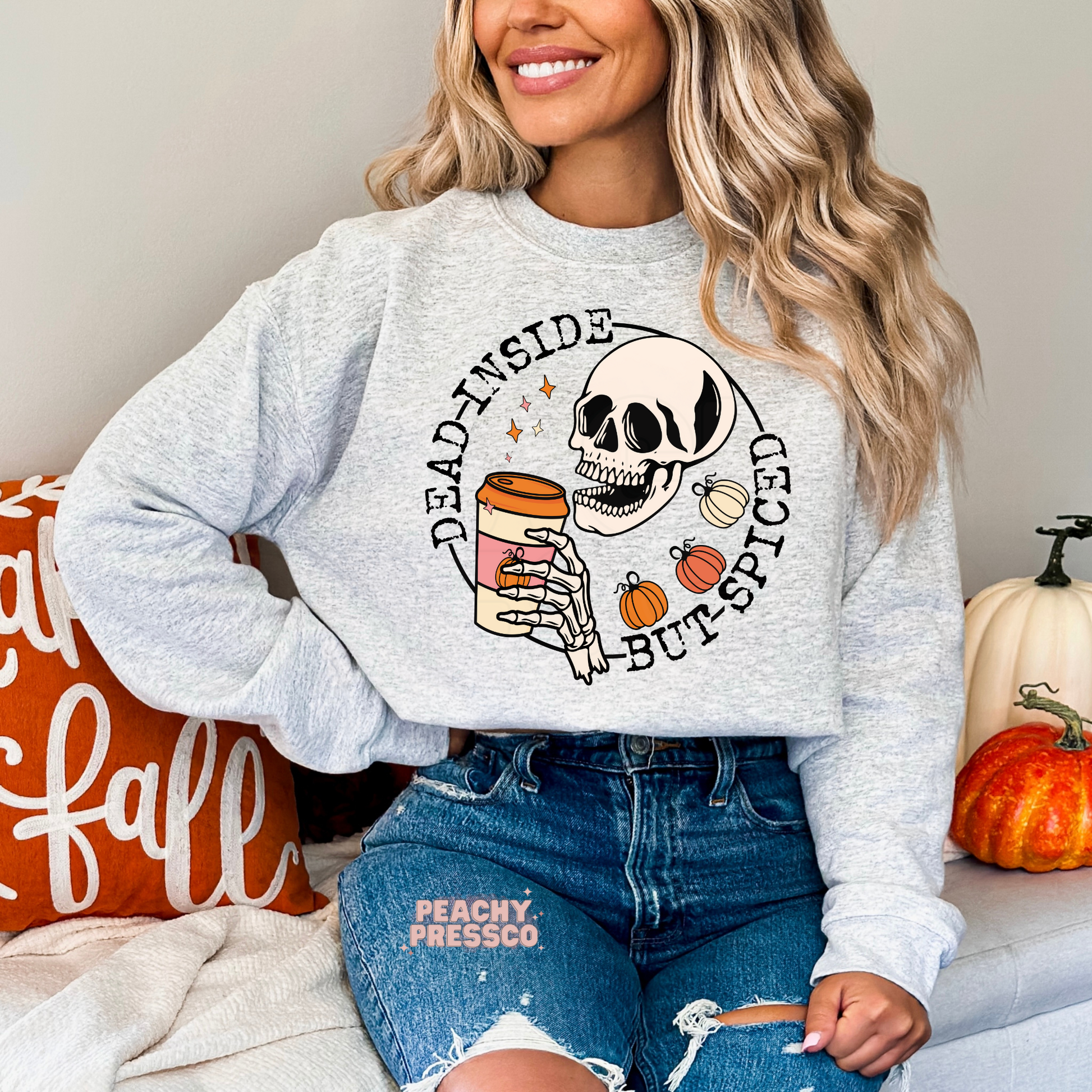 Woman wearing an ash grey crewneck sweatshirt with a skeleton holding pumpkin spice coffee and a funny fall graphic.