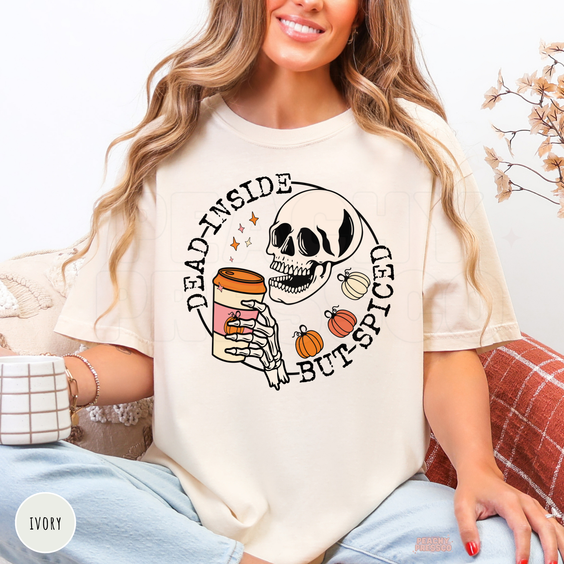 Woman wearing an ivory graphic t-shirt featuring a skeleton, pumpkin spice coffee, and the phrase "Dead Inside But Spiced."